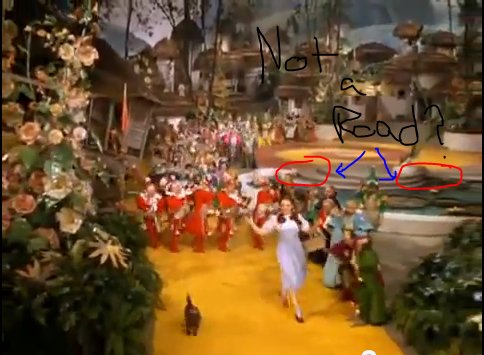 Dorothy and Toto follow the yellow brick road away from the town centre with the crowds following them; the yellow/red spiral of the centre can be seen in the background where the red appears to just end